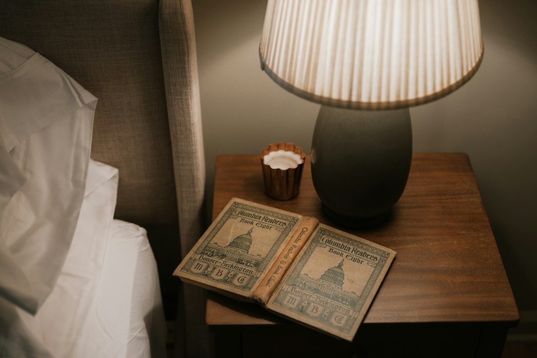 A book beside a lit lamp on a bedside table