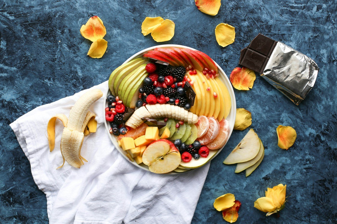 A plate of sliced fruit including banana, pear, apple and berries.