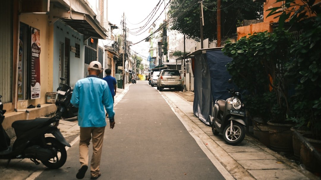 Man walks down a narrow street with buildings.